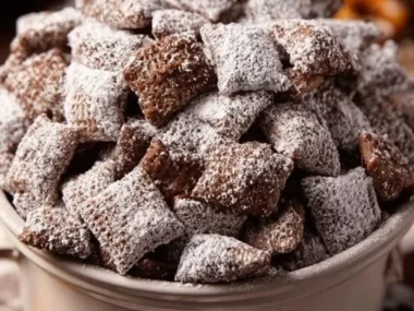 Nutella Puppy Chow Snack Mix in a bowl, topped with chocolate and powdered sugar