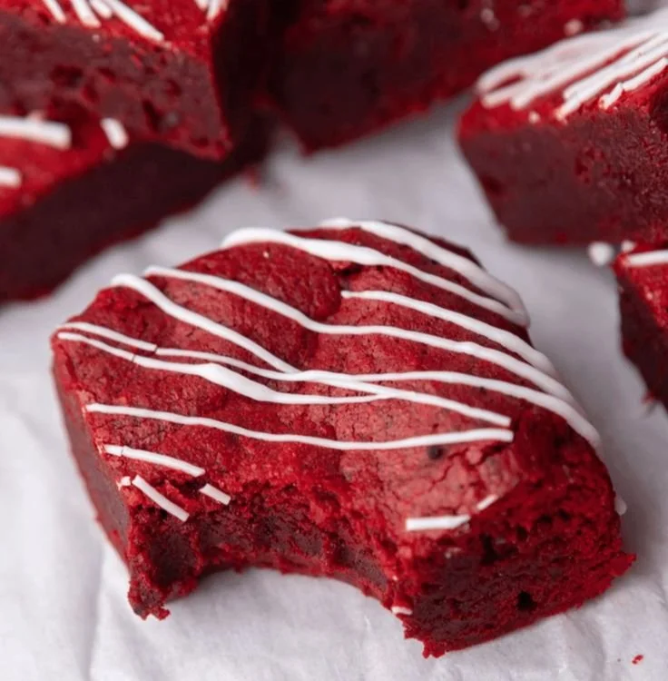 Decadent red velvet brownies topped with cream cheese frosting on a plate.