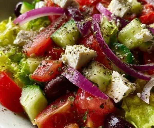 A vibrant bowl of fresh zesty crisp Greek salad with tomatoes, cucumbers, and olives