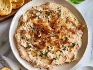 Creamy caramelized onion dip served in a bowl with fresh vegetables and chips