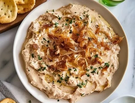 Creamy caramelized onion dip served in a bowl with fresh vegetables and chips