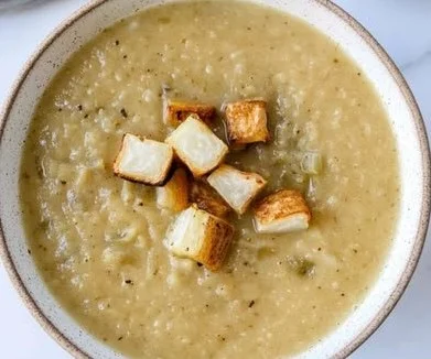 Bowl of creamy Cauliflower Potato Leek Soup garnished with herbs.