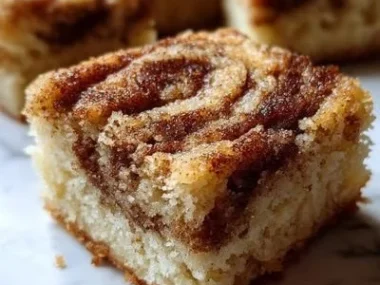 Cinnamon swirl snickerdoodle blondies on a plate, dusted with cinnamon sugar.