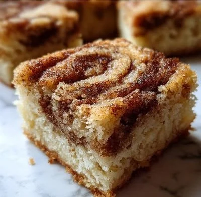 Cinnamon swirl snickerdoodle blondies on a plate, dusted with cinnamon sugar.