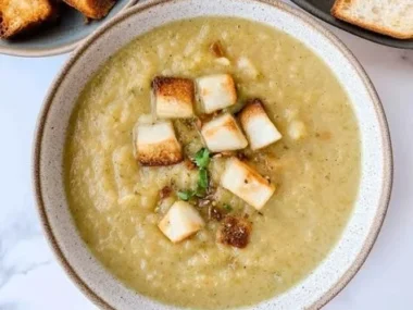 Creamy cauliflower, potato, and leek soup in a bowl topped with fresh herbs.