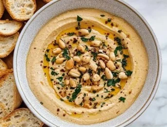 Bowl of healthy peanut butter hummus topped with nuts and served with vegetables