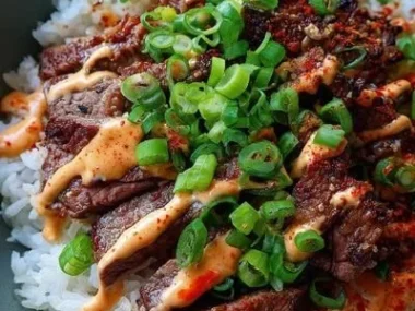 Korean BBQ steak rice bowl with spicy cream sauce garnished with fresh vegetables.