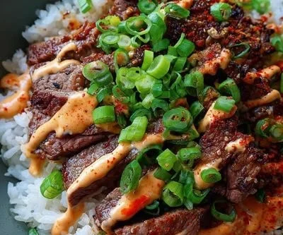 Korean BBQ steak rice bowl with spicy cream sauce garnished with fresh vegetables.