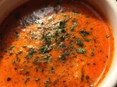 A warm bowl of Roasted Red Pepper Gouda Soup topped with herbs and spices.