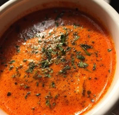 A warm bowl of Roasted Red Pepper Gouda Soup topped with herbs and spices.