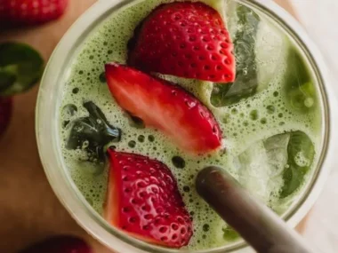 Delicious strawberry matcha latte served in a clear glass with a strawberry on the rim.