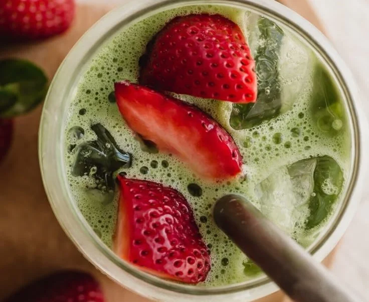 Delicious strawberry matcha latte served in a clear glass with a strawberry on the rim.